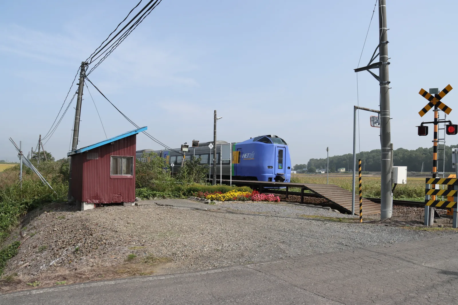 踏切のそばから見た瑞穂駅の待合室、花壇、青い特急列車